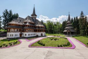 A traditional wooden monastery surrounded by lush gardens and pathways, set in a tranquil forested landscape.