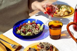 A person dining outdoors, with a glass of rosé wine and a colourful salad on a sunny day.