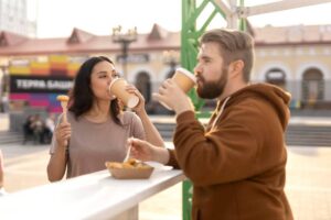 Two people enjoying fast food and drinks outdoors in a lively urban setting.