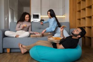 Three friends eating pizza and relaxing in a cozy living room.