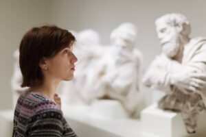 Woman observing classical sculptures in a museum, focusing intently on the artwork.