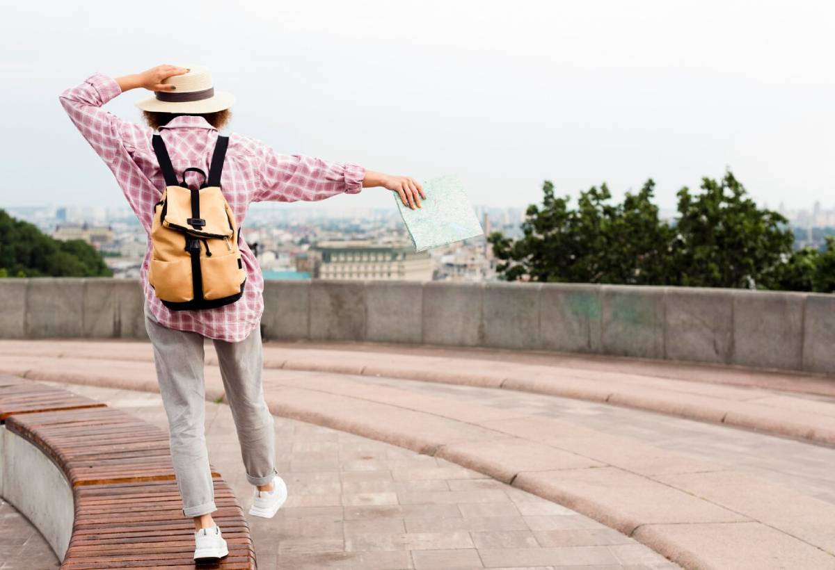  Woman in a hat and backpack holds a map, gesturing expansively with the city backdrop.