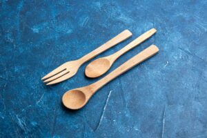 Wooden fork, spoon, and knife set on a blue scratched background.