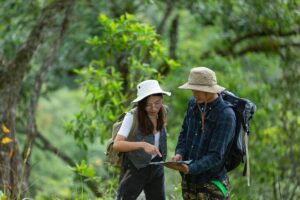 Two hikers with backpacks examining a map in a lush green forest.