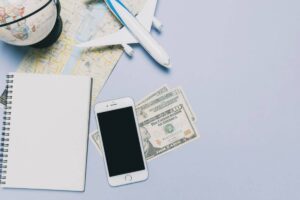 Travel planning setup with maps, globe, airplane, cash, notebook, and a smartphone on a light background.
