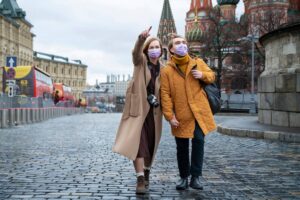 Two people wearing masks and pointing at a landmark in a cobbled street near colorful buildings.