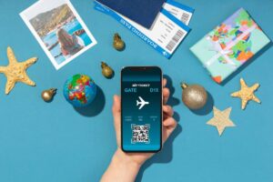 Hand holding smartphone displaying a digital boarding pass, surrounded by travel items and decorations on a blue background.
