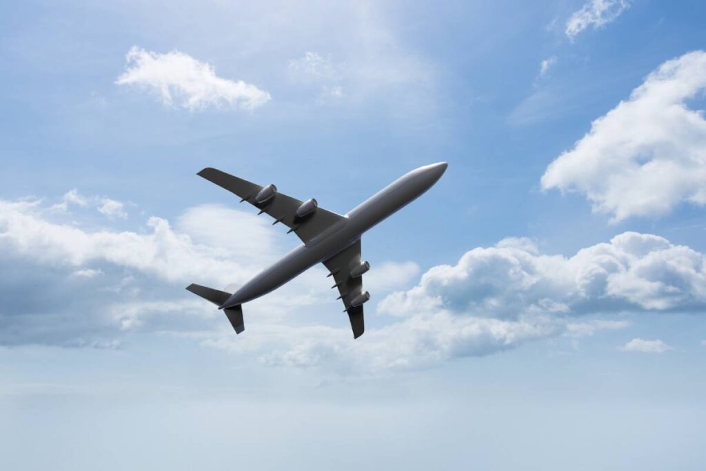 A large passenger jet soaring through a clear blue sky, showcasing its wings and fuselage against the backdrop of clouds.