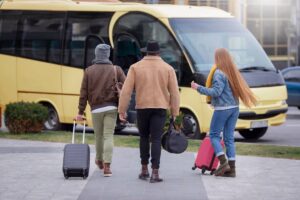 Three people with luggage walking towards a yellow bus.