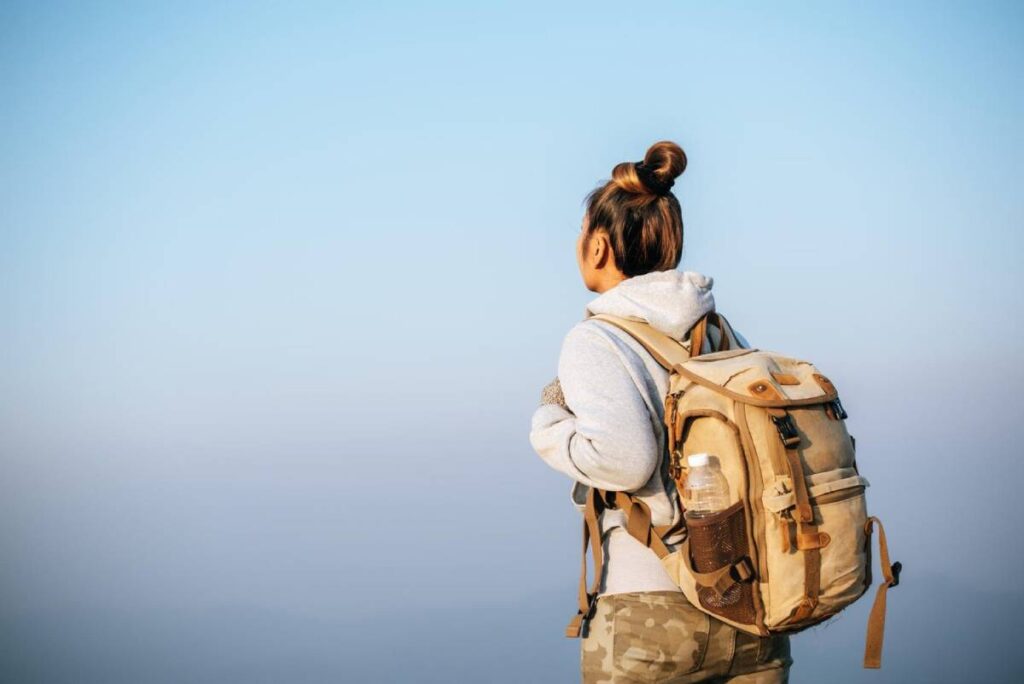 A woman with a backpack standing against a misty, light blue background.