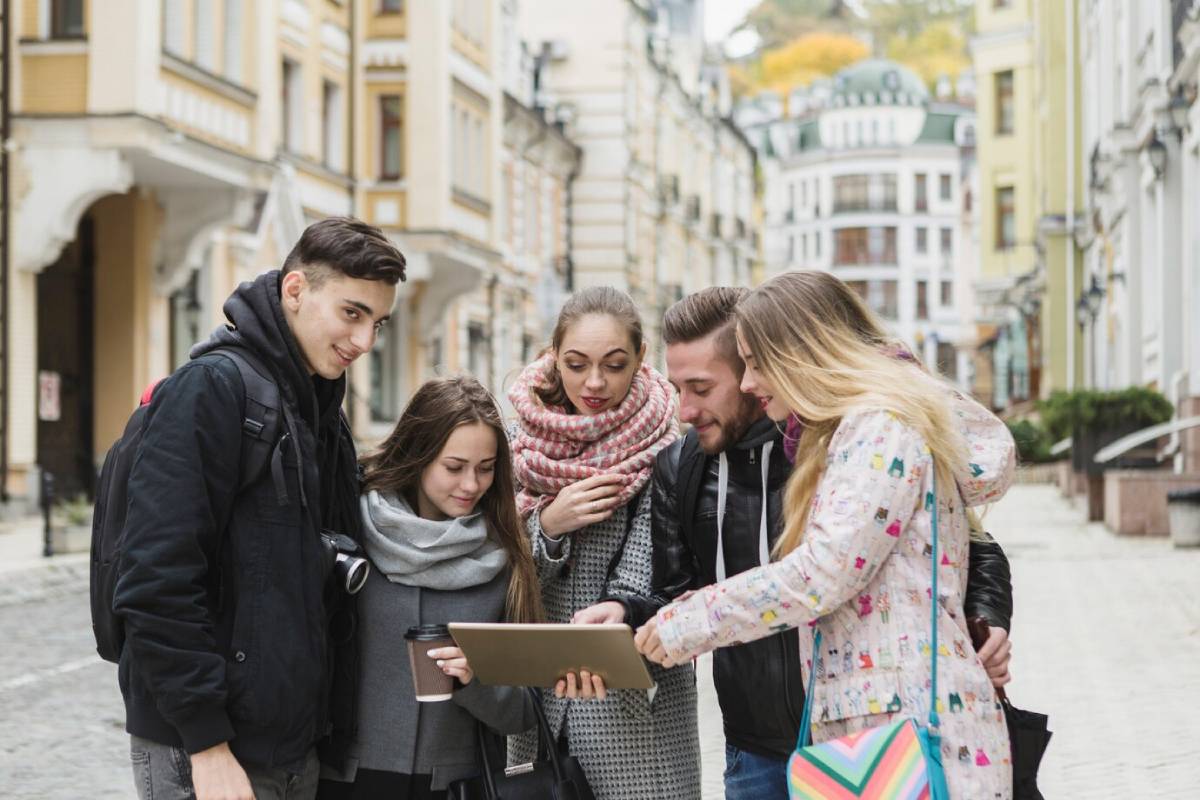 Five young adults sharing a tablet in a quaint European street. 