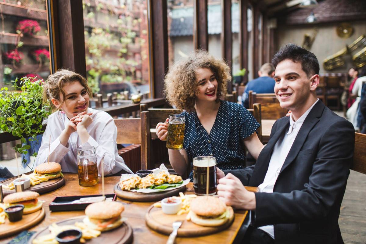  Three friends enjoying drinks and burgers at a lively restaurant terrace.