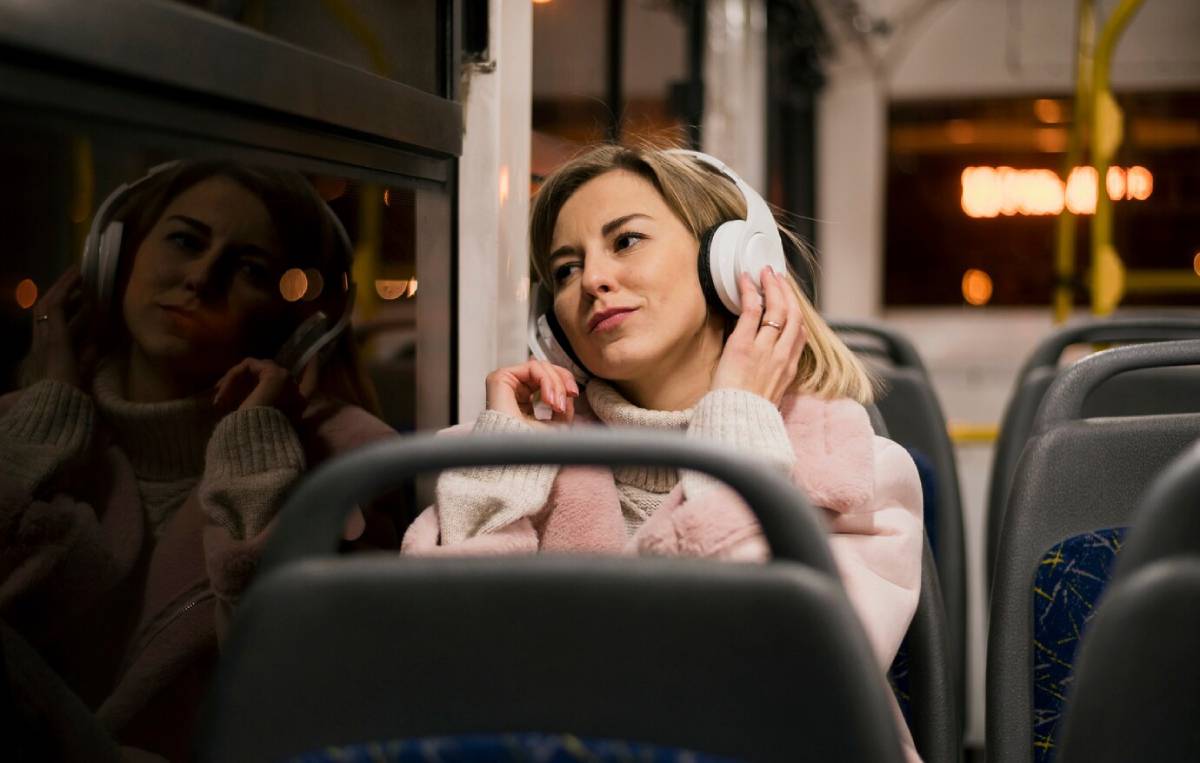 Young woman relaxing with headphones on a bus at night, reflecting in window.