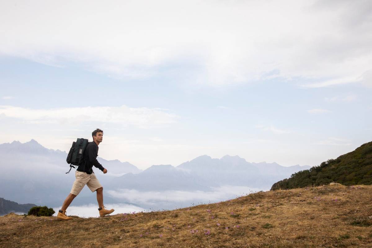  Man hiking on a mountain trail with a backpack, overlooking misty mountain peaks.