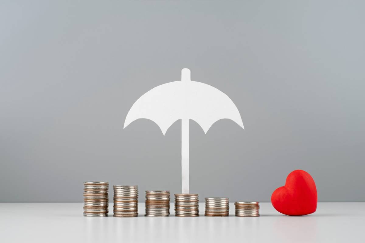  White umbrella above stacked coins with a red heart on a grey background, symbolizing financial security and love.