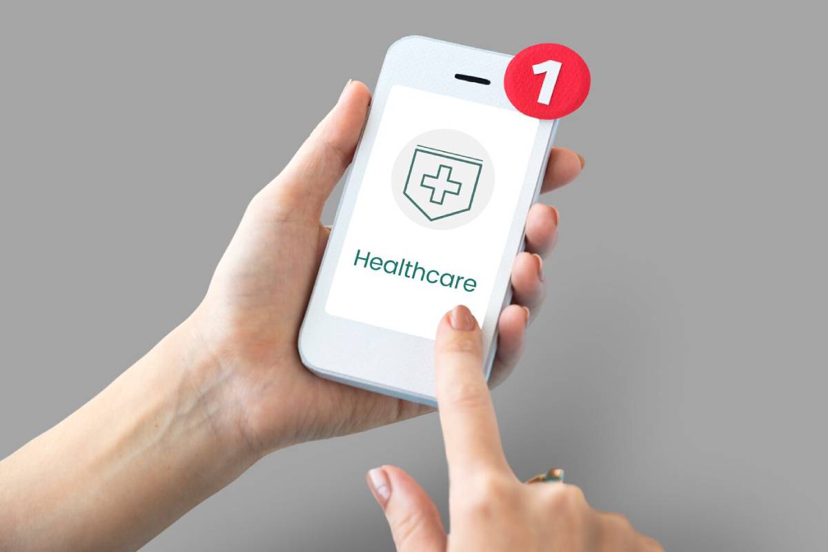 Hand holding a smartphone displaying a healthcare app notification with a medical cross icon. 