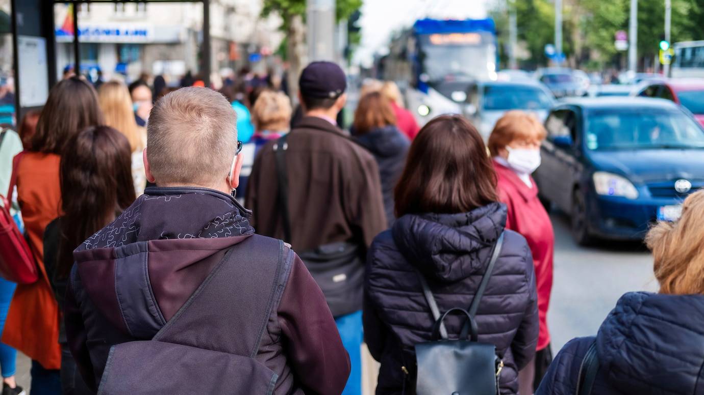 People waiting at a busy city bus stop during daytime.