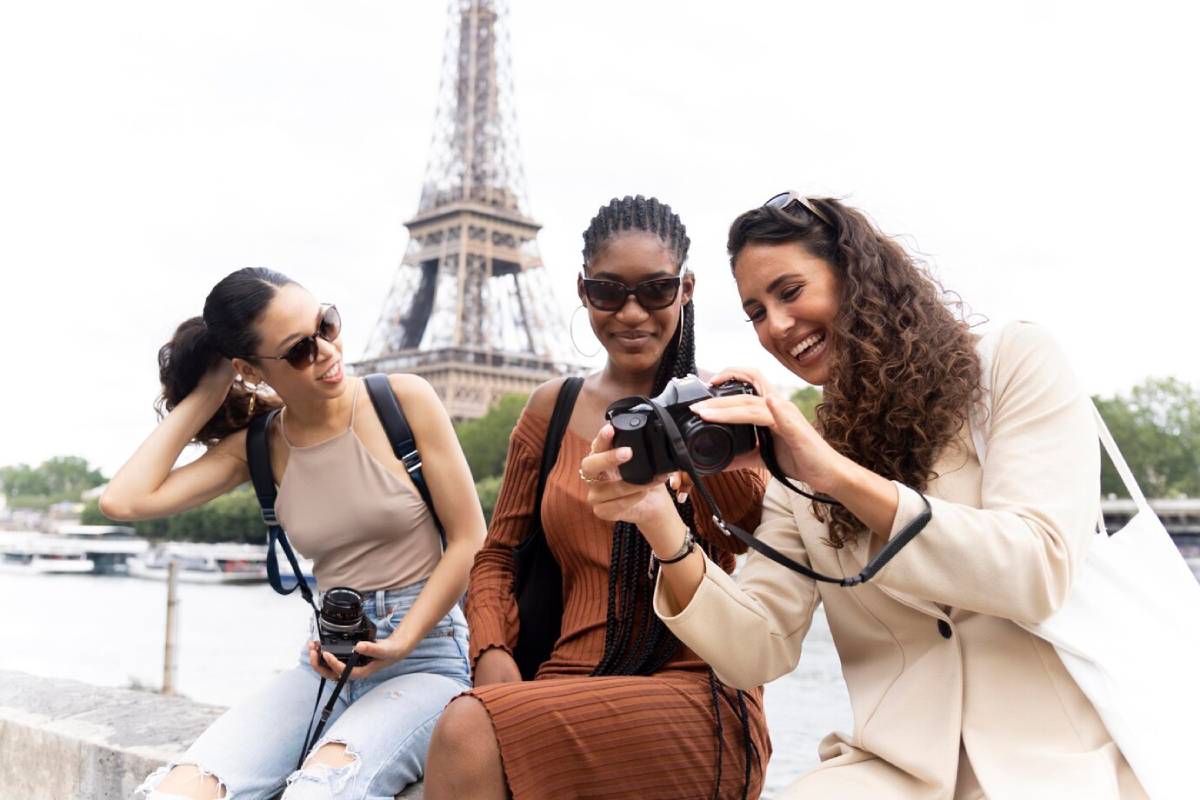 Three women reviewing photos on a camera near the Eiffel Tower in Paris. 