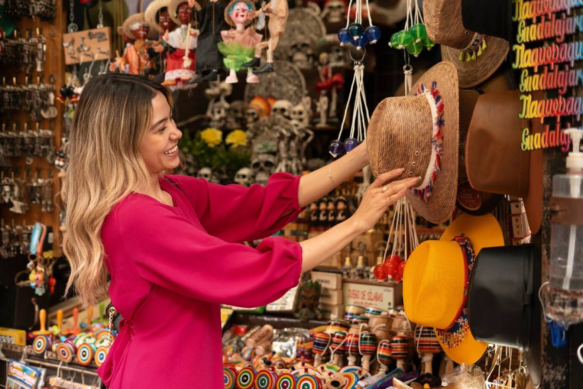  Woman in a pink dress shopping, selecting a hat from a vibrant market stall.