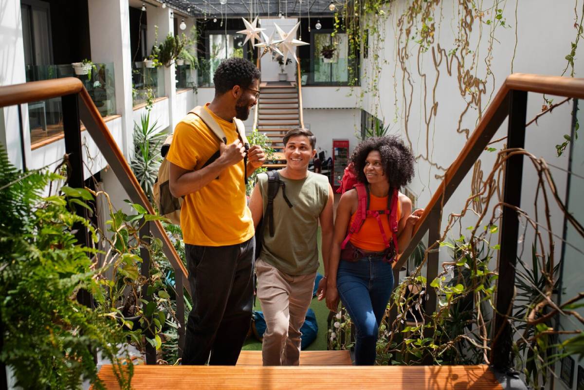  Three friends walking up stairs in a lush indoor garden, chatting and smiling.