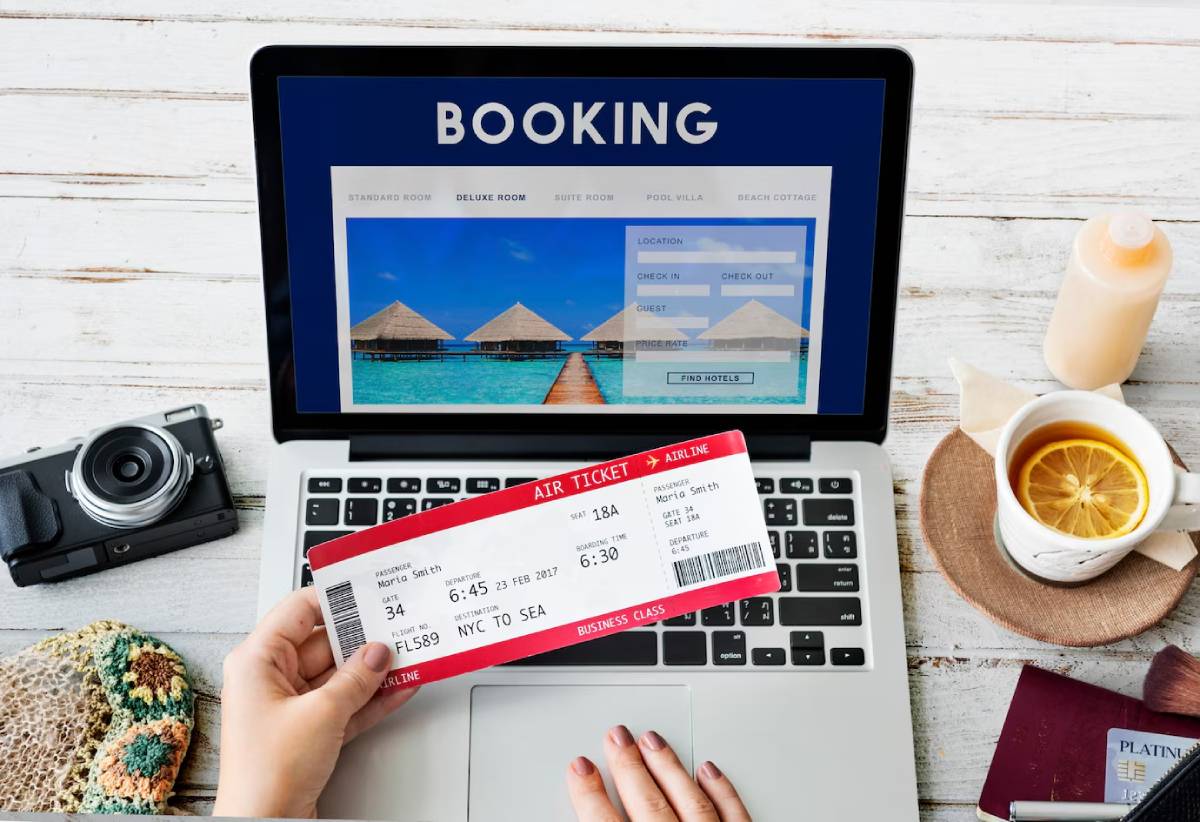  A person booking a holiday online, holding an air ticket with travel essentials on a desk. 