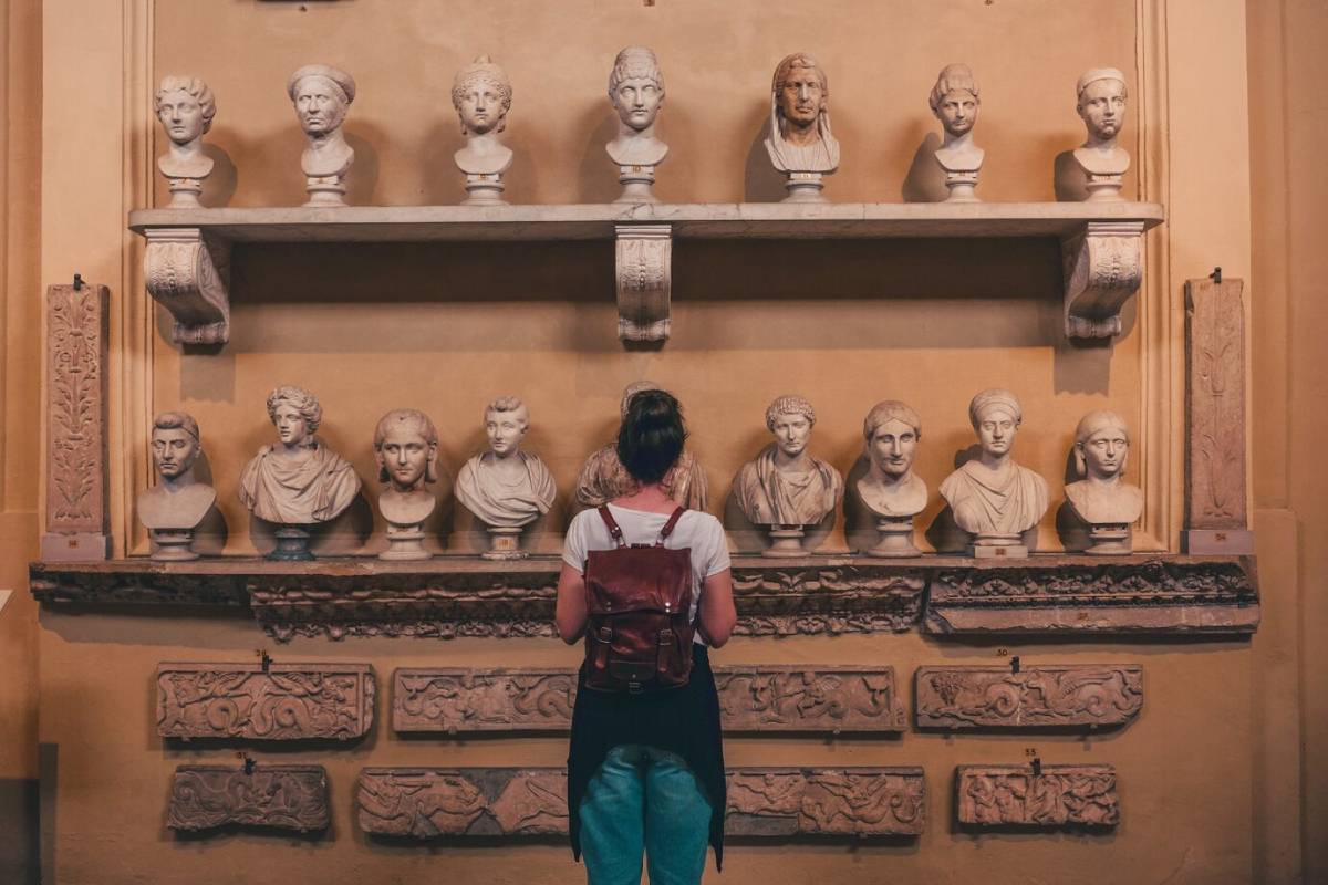  Woman observing a collection of classical busts and sculptures on shelves in a museum.