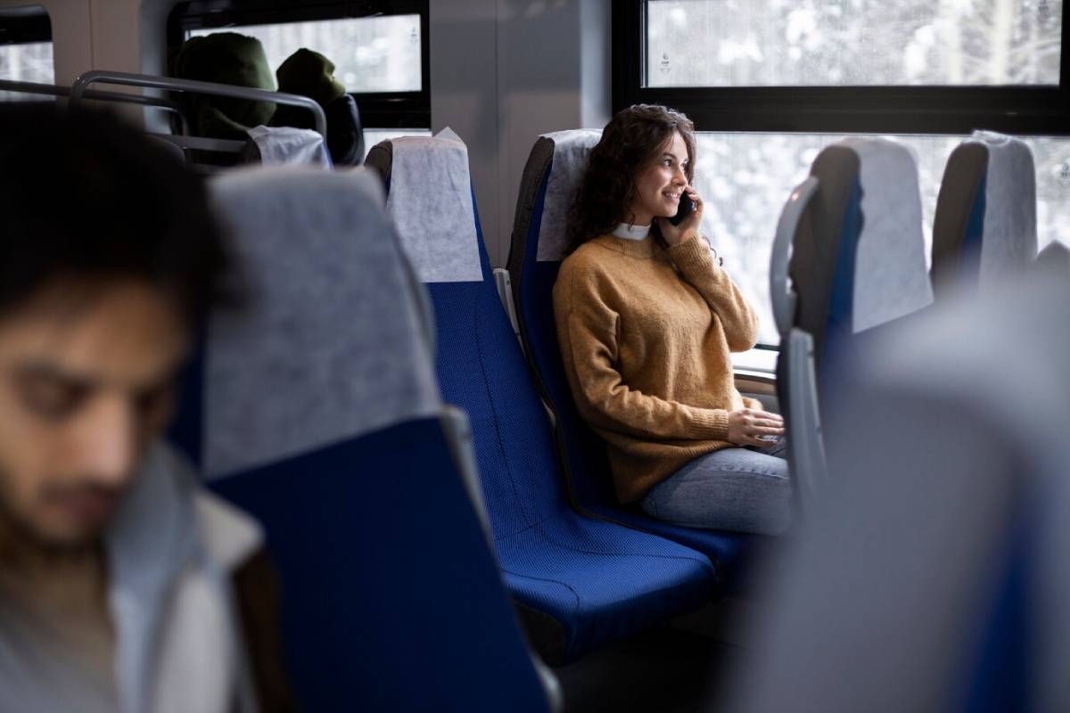 Woman smiling and talking on a phone while sitting in a train, with other passengers around her.