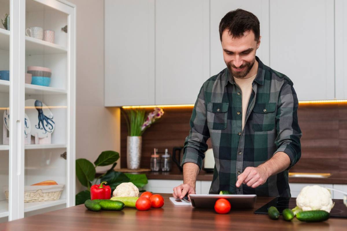  Man using tablet in kitchen with fresh vegetables on the counter.