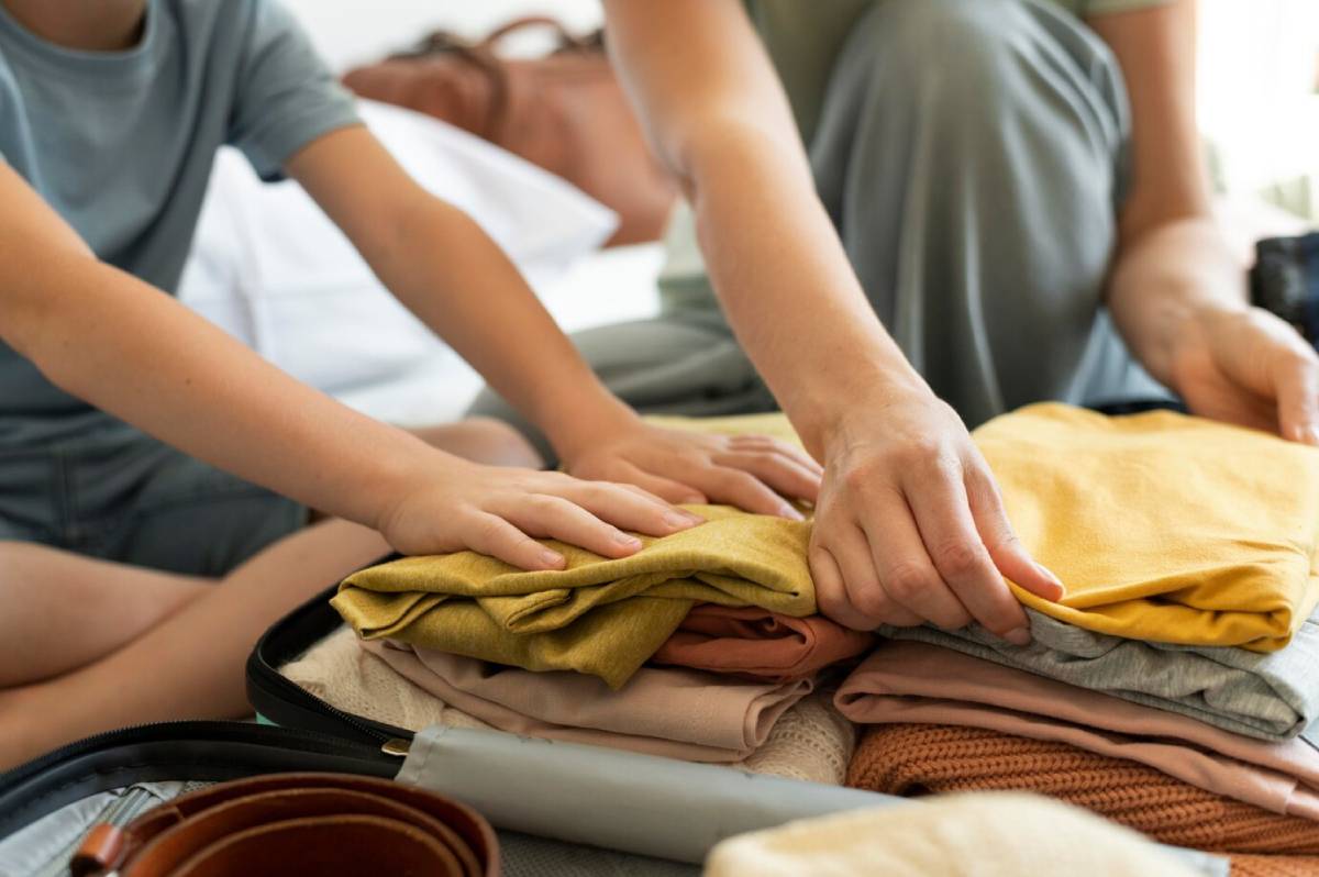 Two people packing clothes into a suitcase, with a focus on their hands arranging folded garments. 