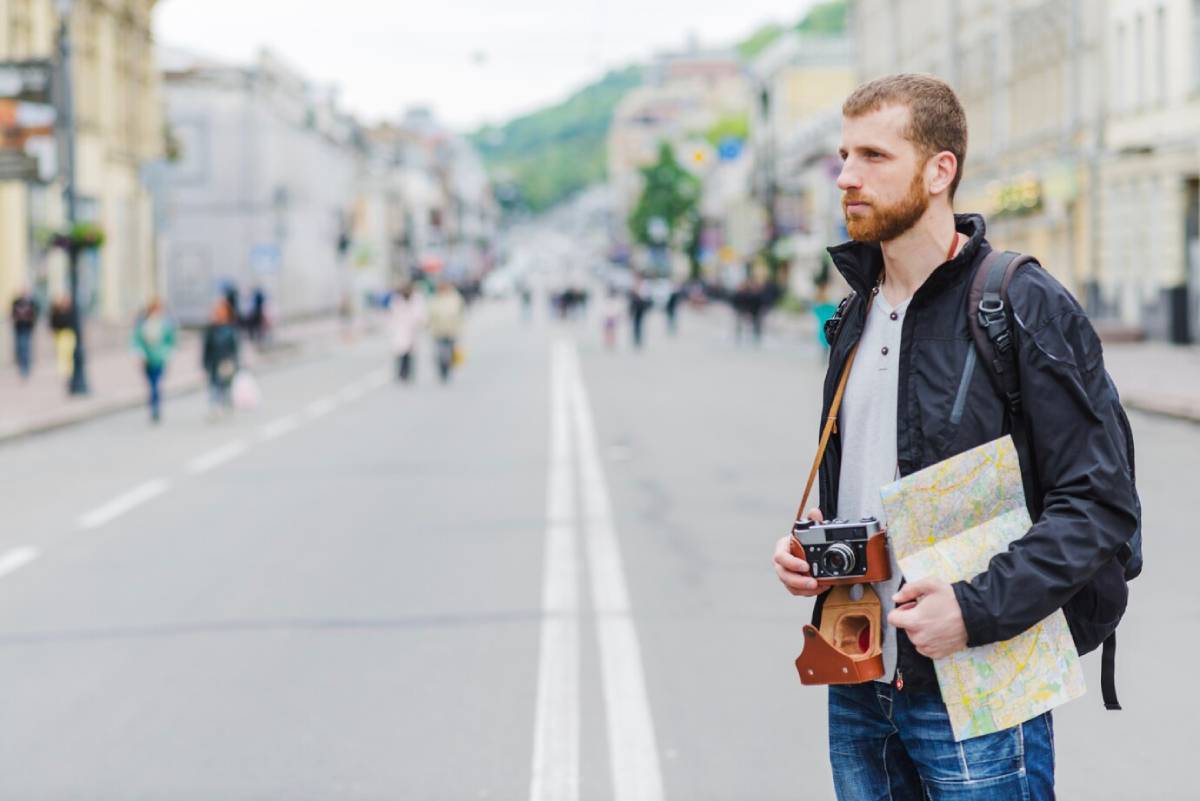 Man with camera and map stands on a city street, looking thoughtful. 