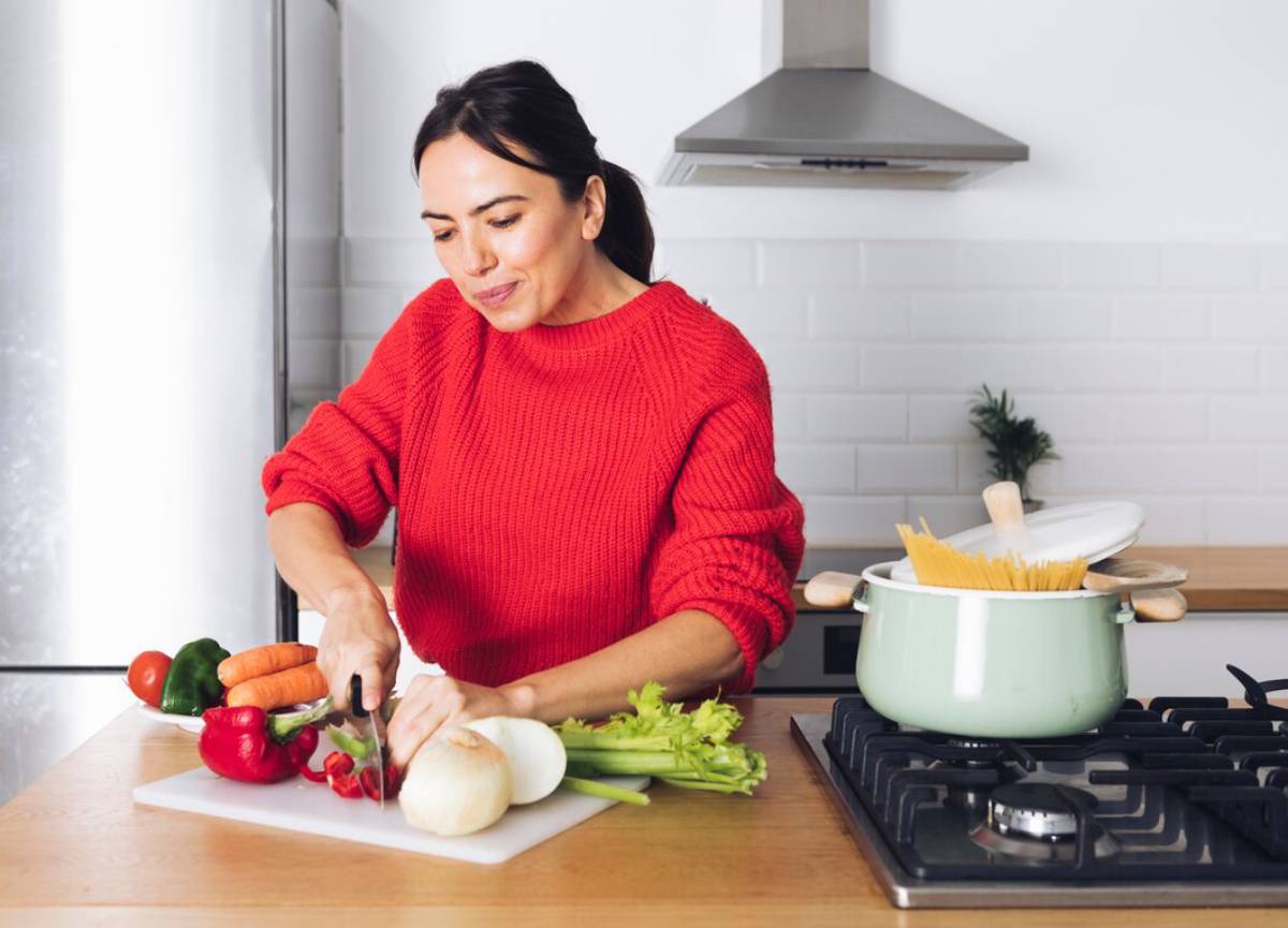  Woman in red sweater chopping vegetables in a modern kitchen.