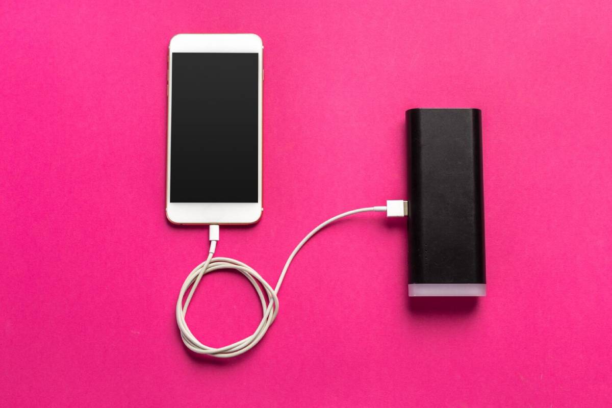  Smartphone connected to a power bank with a white cable on a pink background.