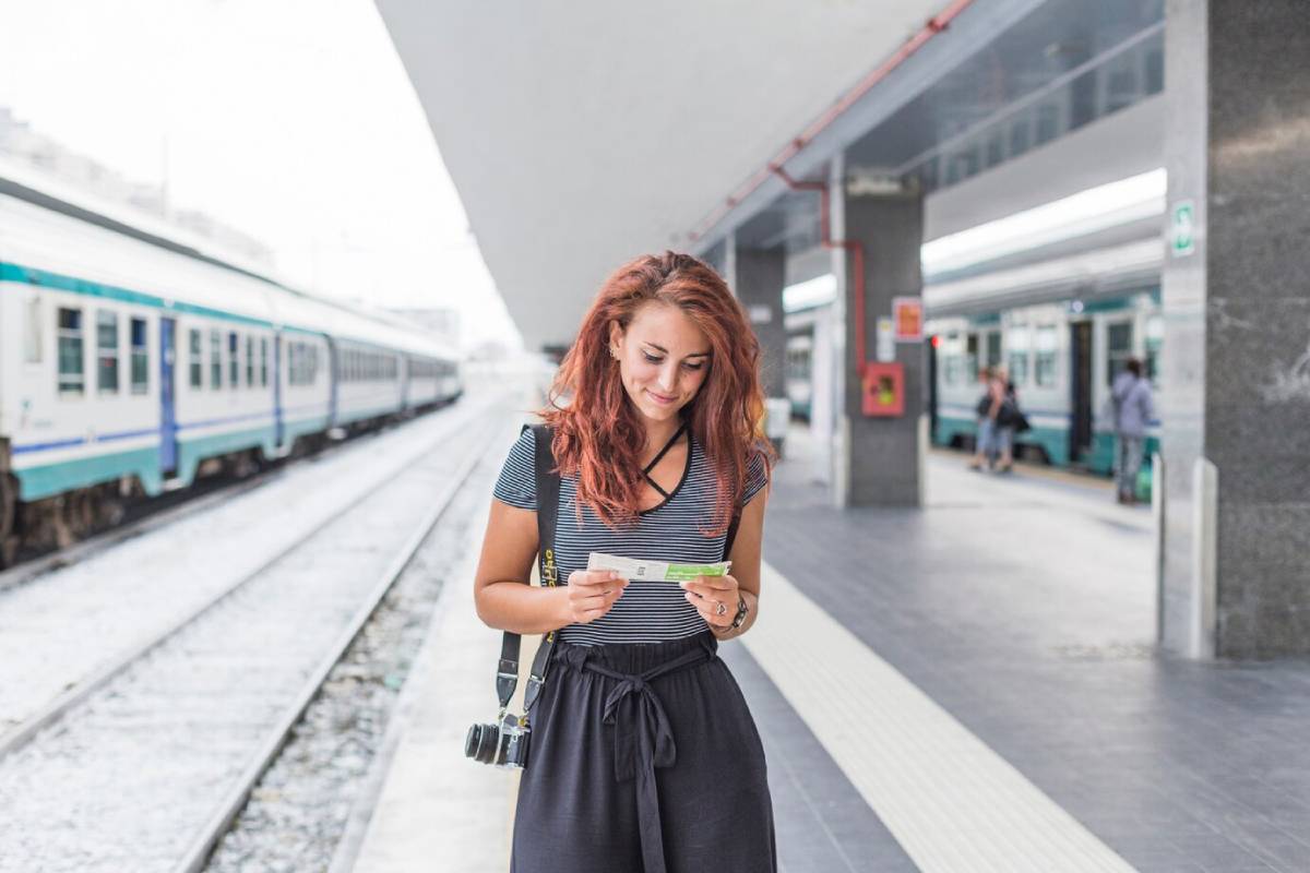 Young woman reading a map at a train station platform, train in background.