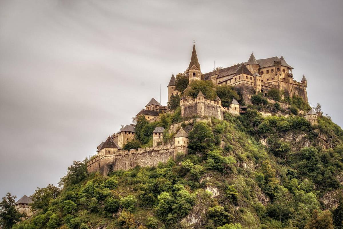  Ancient castle perched on a lush, steep hill under a cloudy sky.