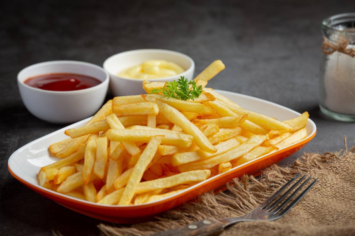 Plate of crispy French fries served with ketchup and mayonnaise on a dark background.