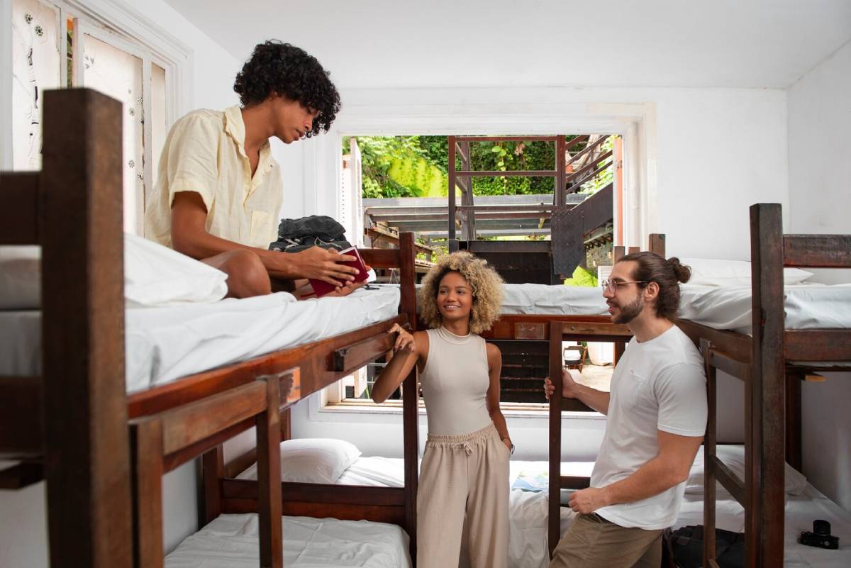  Three friends chatting and packing in a guest house room with bunk beds.