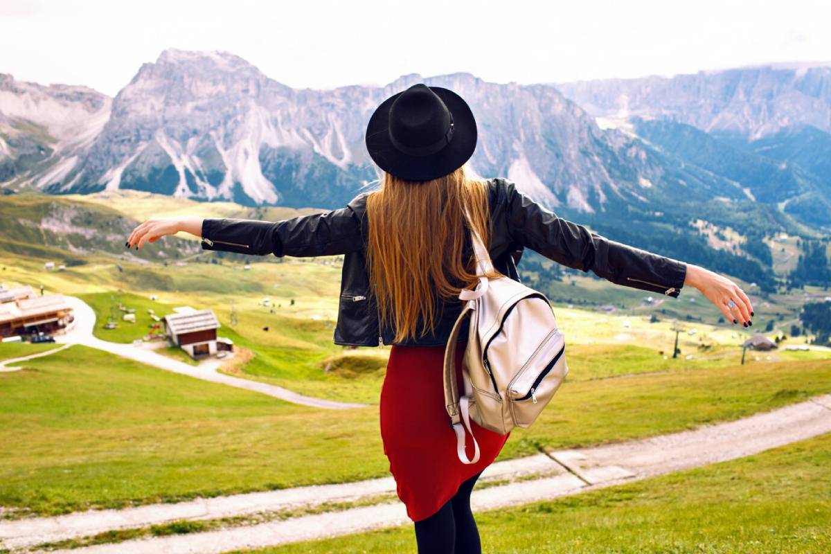  Woman in a hat and leather jacket extending arms in mountainous landscape, feeling of freedom.