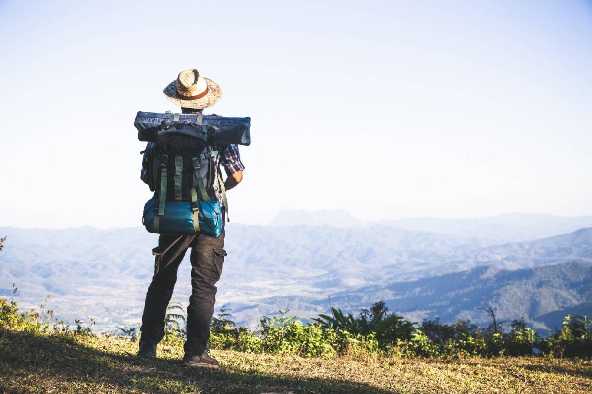  Backpacker with a straw hat overlooking a mountainous landscape under a clear sky.