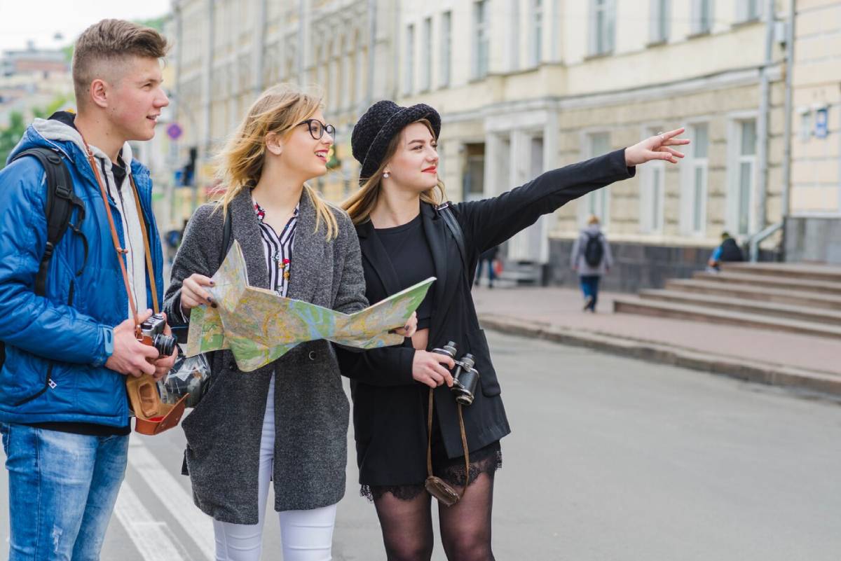 Three young tourists with a map exploring the city, one pointing at something in the distance. 