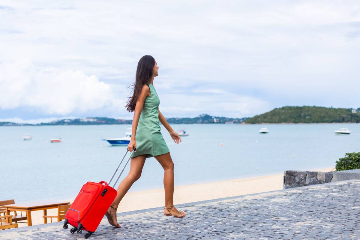  Woman in green dress walking with red suitcase along seaside promenade, overlooking boats on the water.