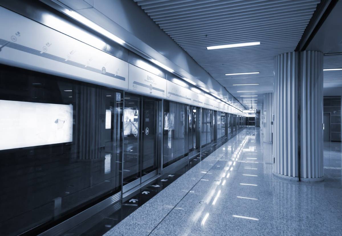 Modern subway station with glass safety doors and minimalistic design, illuminated by overhead lights.
