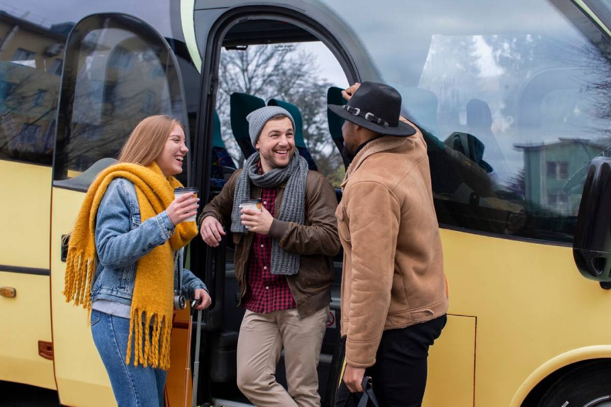  Three friends laughing and talking while boarding a yellow bus, holding cups of coffee.