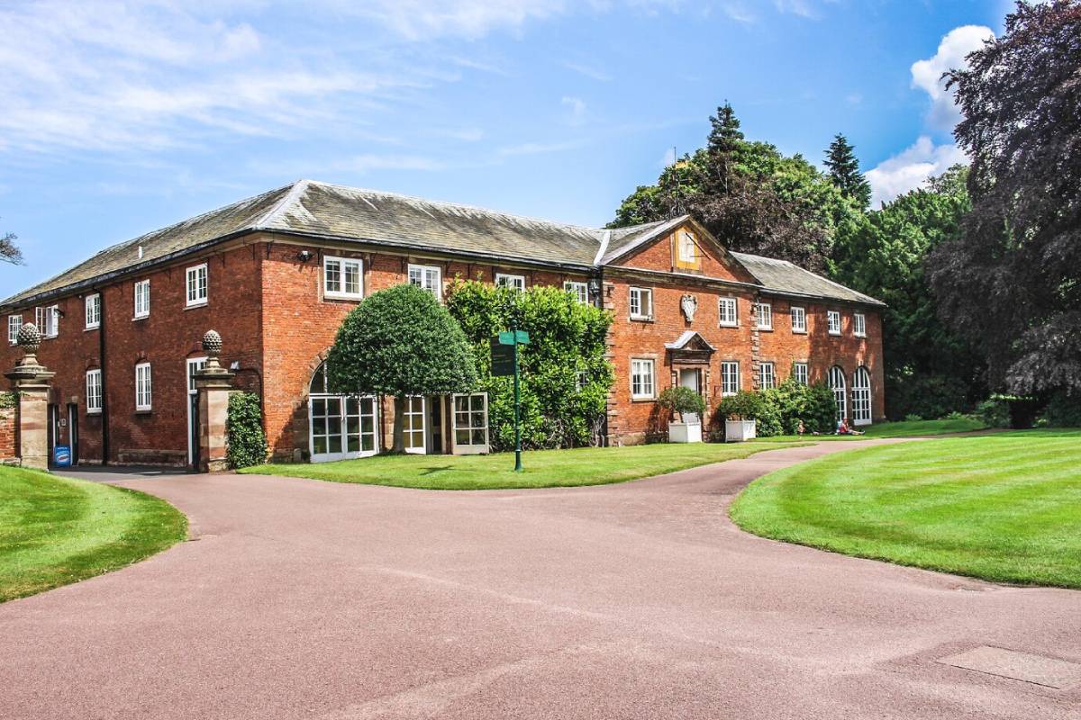  A large, traditional red brick house with a manicured lawn and winding driveway, surrounded by lush green trees.
