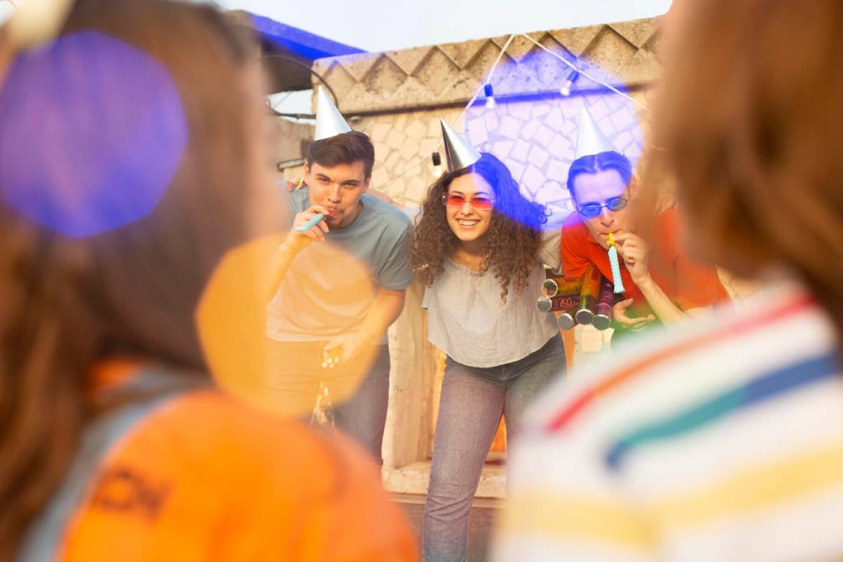 Young adults enjoying a festive party outdoors, blowing party horns and wearing party hats.