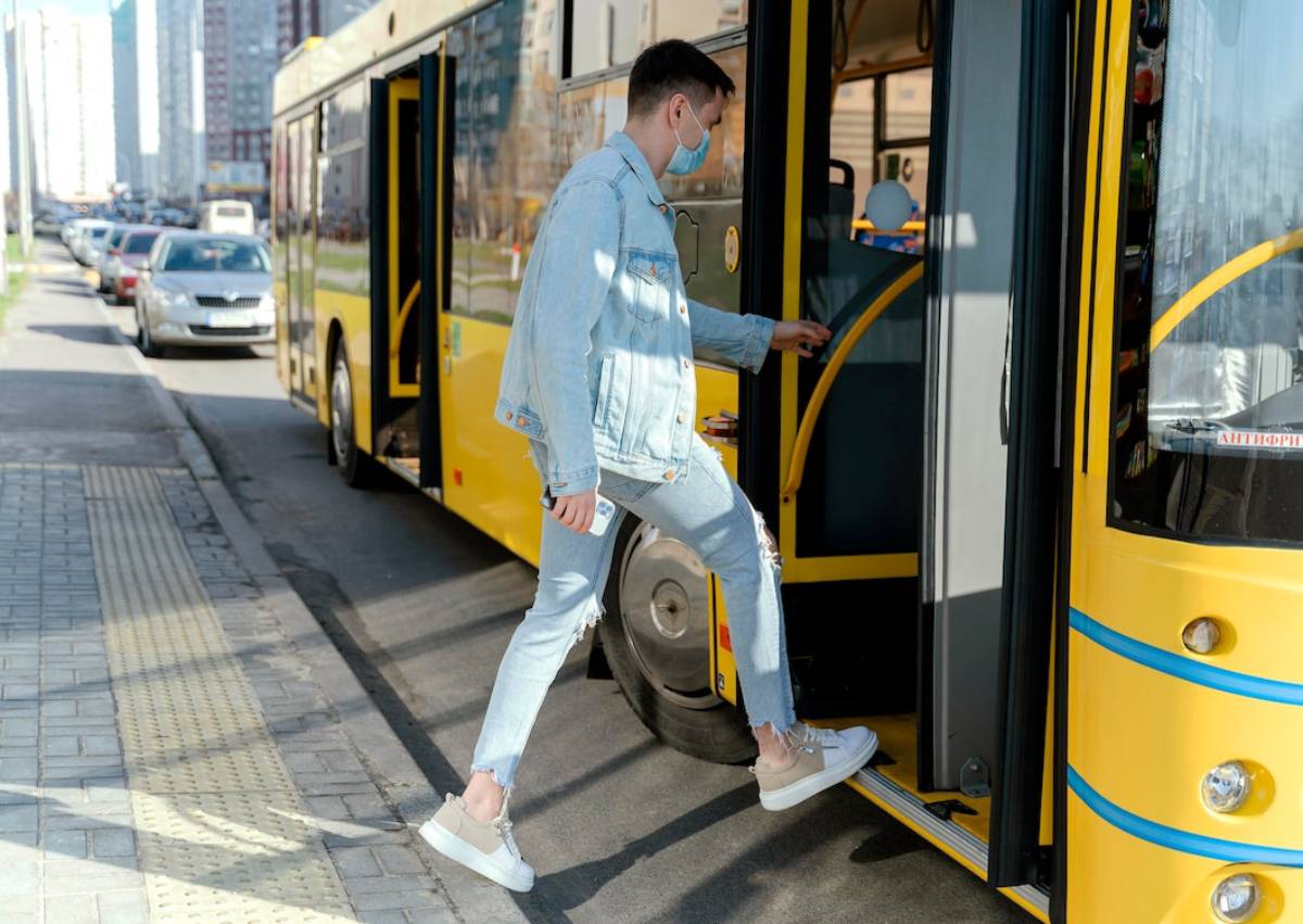 A man in a denim outfit boarding a yellow bus in a city street setting. 
