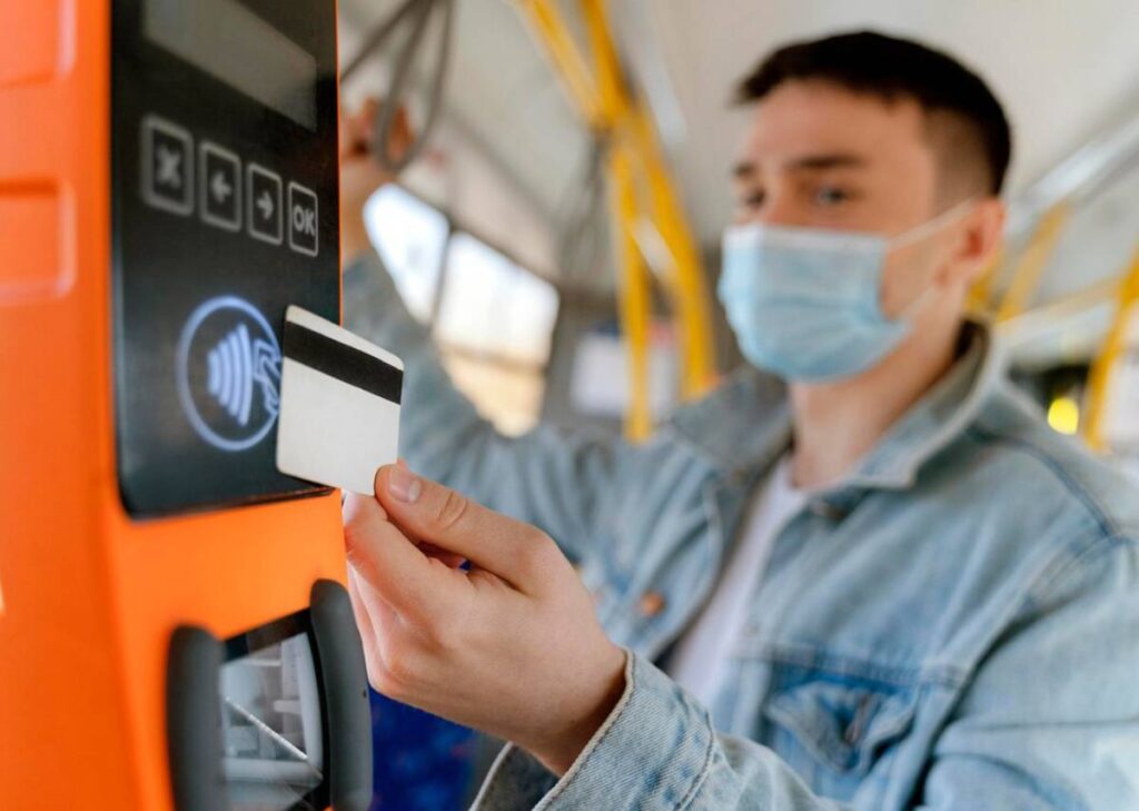 Young man in a face mask using a contactless card to pay on a bus.